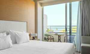 Et hotellrom med oppredd seng og en balkong med utsikt over havet. (AI-generert tekst)