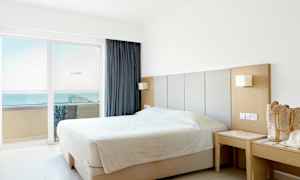 Et hotellrom med en dobbeltseng nær vinduet med utsikt over havet. (AI-generert tekst)