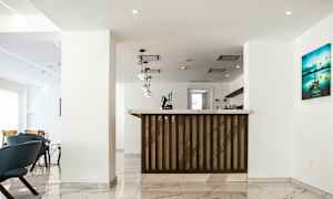 Bilde av en lys og moderne hotellresepsjon med marmorgulv, hengende lamper og en resepsjonsdisk i tre. (AI-generert tekst)