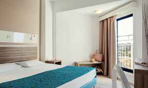 Hotellrom med en oppredd seng, nattbord og en balkongdør. (AI-generert tekst)