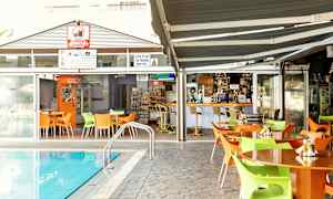 Uteområde med bord og stoler ved et basseng, med en bar og spisested i bakgrunnen. (AI-generert tekst)