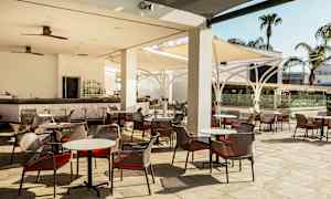 Bilde av en utendørsterrasse med bord og stoler samt en bar. (AI-generert tekst)