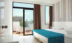 Et hotellrom med en dobbeltseng, et vindu og en balkong med sittemøbler. (AI-generert tekst)