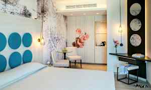 Et hotellrom med moderne design, inkludert en dobbeltseng, bord med stoler, og individuelle designdetaljer som dekorative paneler og belysning. (AI-generert tekst)