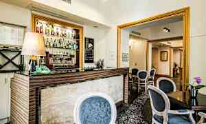 Bilde av en liten hotellbar med forskjellige typer brennevin på hyllen samt en kaffemaskin, omgitt av møblerte sitteplasser. (AI-generert tekst)