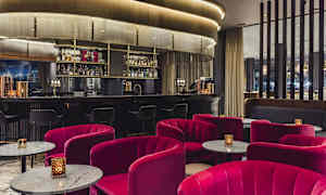 En elegant hotellbar med røde stoler og marmorbord foran en velutstyrt bardisk. (AI-generert tekst)