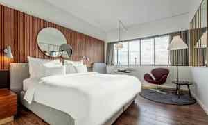 Et moderne hotellrom med en stor seng, et rundt speil på veggen og vinduer med utsikt. (AI-generert tekst)