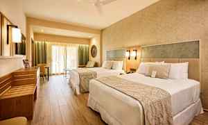 Hotellrom med to senger, sittegruppe og lyse møbler. (AI-generert tekst)