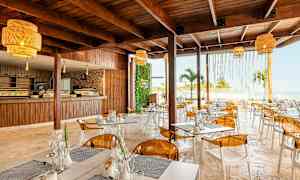 En moderne restaurant med tremøbler, gule lamper og utsikt over havet. (AI-generert tekst)