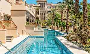 Et langt smalt basseng omgitt av palmer og bygninger med arabisk arkitektur. (AI-generert tekst)