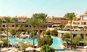 Et hotellområde med et stort basseng omgitt av palmer og parasoller. (AI-generert tekst)