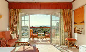 Et hotellrom med åpen balkongdør, sittemøbler og utsikt mot havet. (AI-generert tekst)