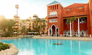 Hotellbygning med rød fasade ved et bassengområde med solsenger og parasoller. (AI-generert tekst)