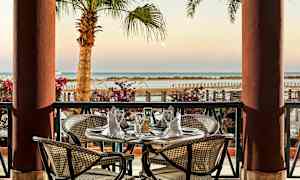 En borddekking på en terrasse med utsikt over havet og palmer. (AI-generert tekst)