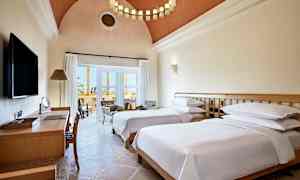 Hotellrom med to enkeltsenger, skrivebord og sittegruppe ved balkongen. (AI-generert tekst)