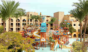 Bilde av en vannpark med sklier og lekeinstallasjoner, omgitt av palmer og hotellbygninger. (AI-generert tekst)