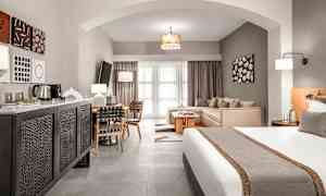 Et hotellrom med en seng, sittegruppe og spisebord, samt moderne interiør. (AI-generert tekst)