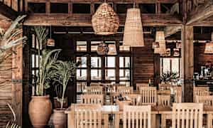 Interiør av en restaurant med tredetaljer, planter og rottinglamper. (AI-generert tekst)