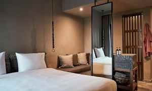 Et soverom med en stor seng, puter, en sofa og et høyt speil. (AI-generert tekst)