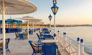 Utendørs servering med blå møbler ved vannkanten under parasoller. (AI-generert tekst)