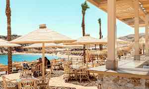 Uteservering med bambusstoler og parasoller nær stranden med blått vann. (AI-generert tekst)