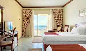 Hotellrom med hvite vegger, to enkeltsenger og en balkong med utsikt over havet. (AI-generert tekst)