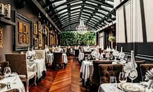Restaurant med elegante bord, duker og glass. Veggene er dekorert med kunst, og rommet har glasstak. (AI-generert tekst)
