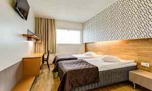 Et hotellrom med to enkeltsenger, et skrivebord og en veggmontert TV. (AI-generert tekst)