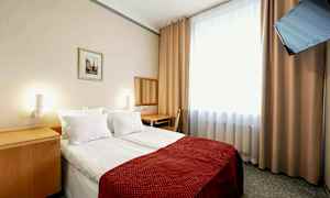 Et hotellrom med en dobbeltseng, rødfarget sengeteppe. Et speil og skrivebord står ved siden av veggen. Et vindu med lyse gardiner og en veggmontert TV finnes i rommet. (AI-generert tekst)