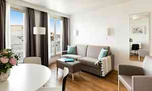 En moderne, lys stue med grå sofa, bord, lenestol og store vinduer som slipper inn naturlig lys. (AI-generert tekst)