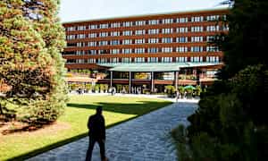 En bygning med en moderne inngang omgitt av grøntområder og gangveier. (AI-generert tekst)