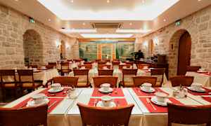 En spisestue med dekkede bord og stoler, omgitt av steinvegger og dekorert med et veggmaleri. (AI-generert tekst)