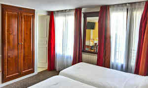 Et hotellrom med to senger, hvite laken og en tretrekk ved siden av et vindu med røde gardiner. (AI-generert tekst)