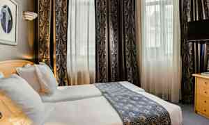 Et hotellrom med to enkeltsenger, lyse gardiner og et dekorativt sengeteppe. (AI-generert tekst)