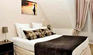 Et soverom med en seng, puter, kunst på veggen og gardiner. (AI-generert tekst)