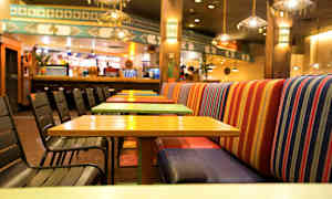 En restaurant med fargerike bord og stoler, samt stripete benkeseter. (AI-generert tekst)