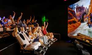 En gruppe mennesker sitter i en interaktiv simulator med en stor skjerm som viser en naturscene med fjell og elv. (AI-generert tekst)