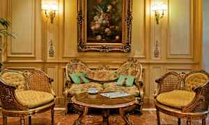 Et elegant innredet rom med en overdådig dekorert sofa, to matchende lenestoler og et salongbord foran. Oljemaleri på veggen over sofaen. (AI-generert tekst)