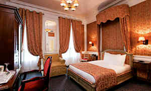 Et hotellrom med en klassisk interiørstil, med en dobbeltseng, røde gardiner og en lenestol. (AI-generert tekst)