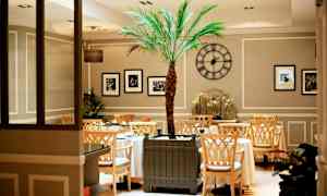 Inne i en elegant kafé med et sentralt plassert palmetre og dekorative detaljer. (AI-generert tekst)