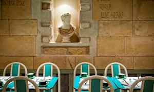 Bildet viser en restaurant med turkise bord og stoler samt en hvit skulptur i en nisje på veggen. (AI-generert tekst)