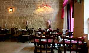 Et restaurantområde med bord og stoler, samt dekorasjonsplanter foran en steinvegg. (AI-generert tekst)