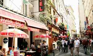 En livlig gate i en by med uteserveringer og skilt fra forskjellige restauranter og hoteller. (AI-generert tekst)