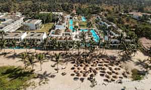 Luftfoto av en resort med bassenger, tropiske palmer og strand med parasoller. (AI-generert tekst)