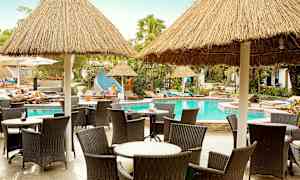 Stoler og bord ved et basseng med stråtak. (AI-generert tekst)