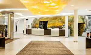 Resepsjon i en moderne hotellobby med et stilig gyllent interiør og lys innredning. (AI-generert tekst)