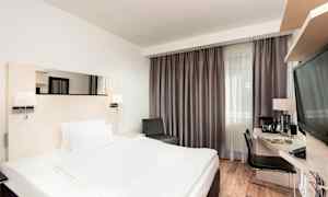 Et hotellrom med en dobbeltseng, skrivebord og stol, samt et stort vindu med gardiner. (AI-generert tekst)