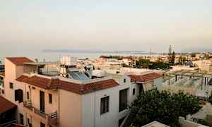 Utsikt over hustak i en kystby med havet og fjell i bakgrunnen. (AI-generert tekst)