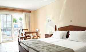 Et hotellrom med to senger, et trebord og stoler, samt en balkong med utsikt over bassengområdet. (AI-generert tekst)