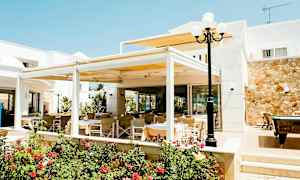 Utendørs serveringsområde med bord og stoler ved en bygning, omgitt av blomster og planter. (AI-generert tekst)